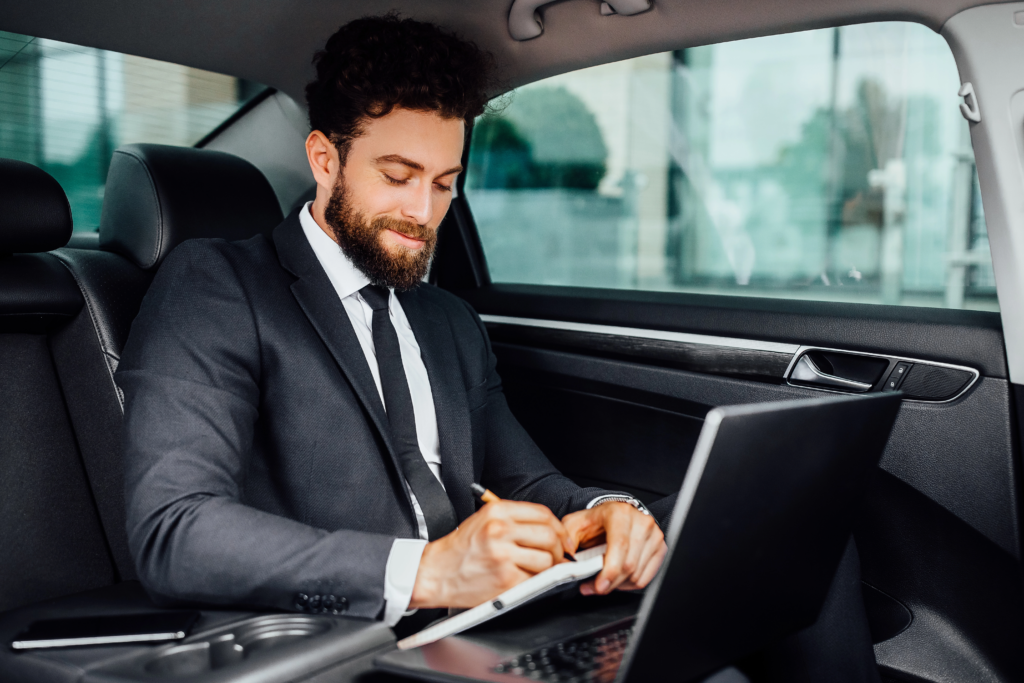 handsome-bearded-smiling-businessman-working-backseat-car-makes-notes-notebook-from-his-laptop